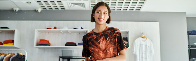 young successful asian fashion designer smiling at camera in modern print studio, horizontal banner