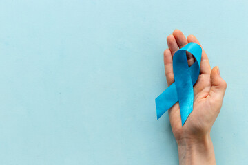 Blue ribbon symbol of colon or prostate cancer with hands. Medical support and prevention