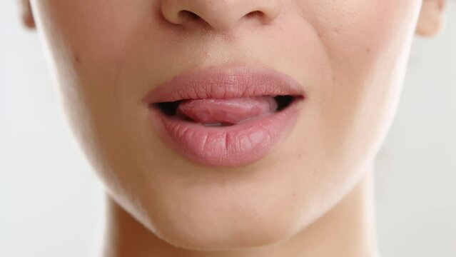 Close up of lower part of face of young slim woman with delicate facial features. lipstick of natural color, moving tongue seductively along white teeth. High quality 4k footage