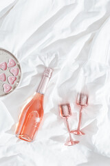 Pink champagne glasses with metal shiny, bottle of rose sparkling wine ,pink candle hearts on bed....