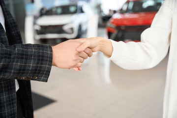 People shaking hands in dealership after signing documents of new car
