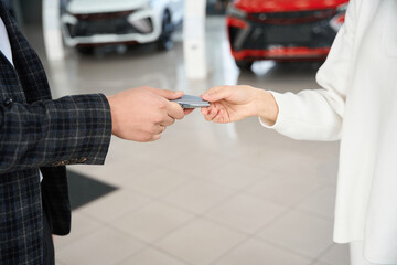 Man dealer giving car key to woman in automotive dealership showroom