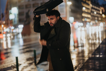 A good-looking businessman standing in a busy city at night, covering his head with laptop case...