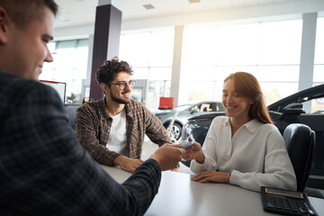 Car seller giving car keys to new owners congratulating with successful purchase
