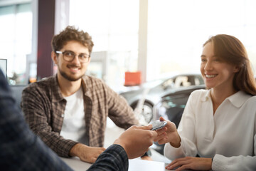 Man and woman sitting in dealership office receive keys of their new automobile