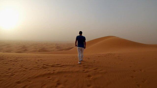 Man walking in the dunes of the Merzouga desert with sandstorm at sunset