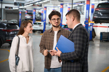 Salesman giving keys of new car to young man and woman in modern dealership