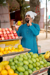 Young Indian fruit seller showing or talking phone at the camera, mixing tradition with technology.