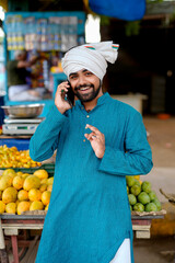 Obraz premium Young Indian fruit seller showing or talking phone at the camera, mixing tradition with technology.