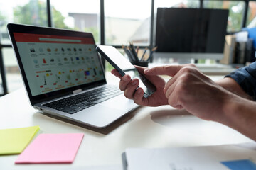 Male businessman, independent entrepreneur uses mobile phone through smartphone application to chat online. Online booking, podcast, cashback, business transactions via mobile phone in modern office.