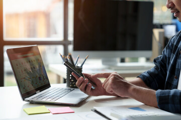 Male businessman, independent entrepreneur uses mobile phone through smartphone application to chat online. Online booking, podcast, cashback, business transactions via mobile phone in modern office.