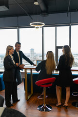 Positive colleagues work on profitable offer from client at wooden table. Man and women in business suits discuss working moments