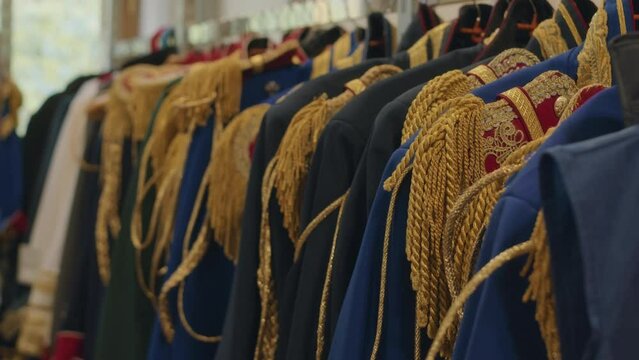 No people shot of many blue male ceremonial jackets with golden aiguillettes hanging on racks in dressing room