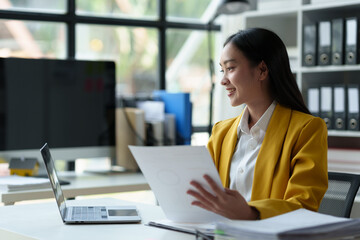 Asian businesswoman, investor, insurance salesperson pointing at data sheet. Earnings. Chart showing financial growth in real estate business based on data from laptop. Modern working lifestyle.