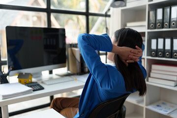 Asian businesswoman stretches her arms and stretches to relax tired muscles from working at a desk all day in the office, concept of success in startup business.