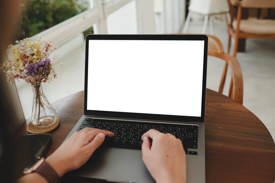 Mockup image of hand using laptop with blank white screen on vintage wooden table near glass windows in cafe