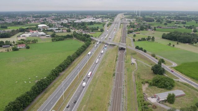 This drone footage offers a sweeping view of a busy E19 Antwerp Breda highway interchange in Brecht, with multiple lanes of traffic flowing smoothly against a backdrop of lush green fields. The