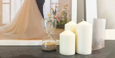 Big candles are beside the sand clock on a dusty dark table