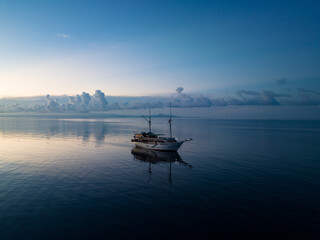 A phinisi schooner, used as a diving live aboard, drifts in calm seas at sunrise near Ambon,...