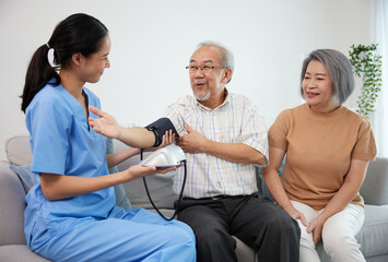 caregiver or nurse measure blood pressure to senior man on sofa - obrazy, fototapety, plakaty