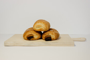Tres napolitanas en una tabla de madera sobre fondo blanco. Napolitanas de chocolate y crema....