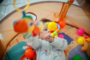 The adorable baby is happily playing with colorful balls inside a toy basin.