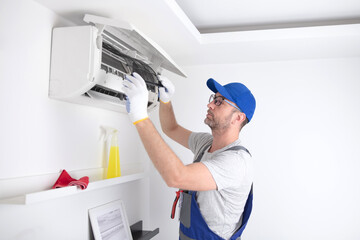 Service guy cleaning and maintaining air condition unit. - obrazy, fototapety, plakaty