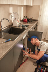 Plumber fixing and repairing water pipes under the kitchen sink.