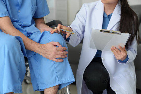 A Caring Female Doctor Provides Medical Care To A Male Patient In A Wheelchair Who Has Knee And Ankle Pain Due To Overwork. Shock Received Medical Attention From Doctors At The Hospital.