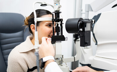 An unrecognizable ophthalmologist uses a slit lamp with a camera to examine a woman's eye....