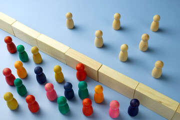 Diversity and immigration. Multi-colored figures are separated from wooden ones by a wall.
