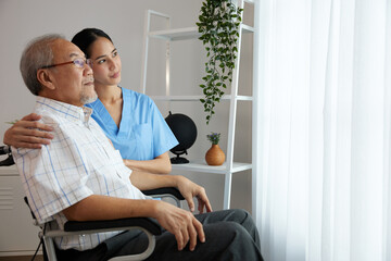 nurse or caregiver beside elderly man sitting on wheelchair and looking outside at home
