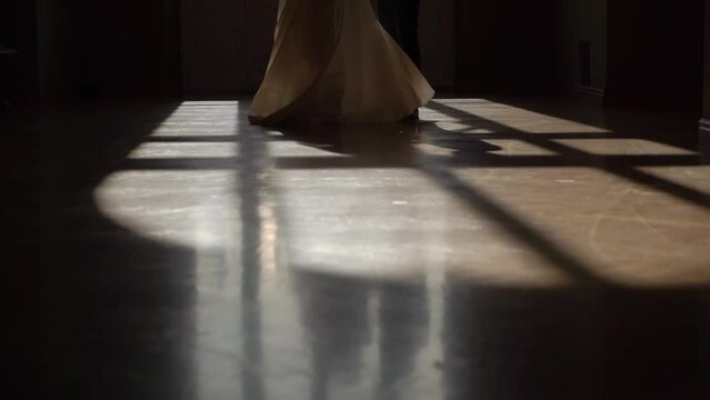 The bride in a long wedding dress is spinning, tearing the hem of her dress. Slowmotion indoors. Heeled shoes, groom in suit.