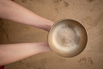 Top view of a woman holding a Tibetan singing bowl with two hands at the beach