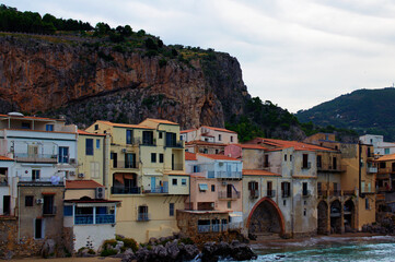 Fototapeta na wymiar Picturesque landscape view of coastline in ancient city Cefalu. Colorful buildings at the sandy beach. Waves of tranquil water splashing against the walls. The Tyrrhenian Sea, Cefalu, Sicily, Italy