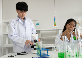 Asia kid boy in science uniform funny learning study science of use microscope and test chemical