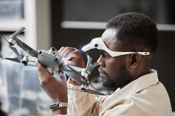 Side view portrait of African American man assembling drone and wearing flashlight gear in tech...