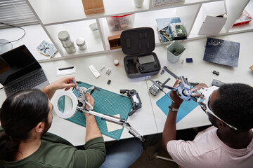 Top view at two people fixing quadcopter drones at workstation in tech repair shop, copy space