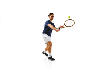 Young athletic man, tennis player in motion, hitting ball with racket isolated over white background. Dynamic game. Concept of professional sport, competition, game, math, hobby, action