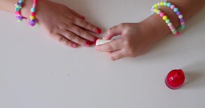 Little girl make manicure and painting nails with red nail polish at home.