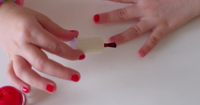 Little girl make manicure and painting nails with red nail polish at home.