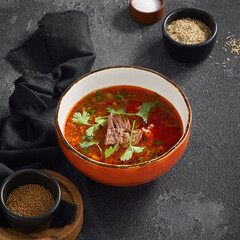 Authentic Georgian Harcho soup, rich with beef and fresh cilantro leaves, served in a rustic orange bowl on a dark grey surface