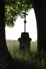 A monument with a cross of Jesus Christ between two trees by the field