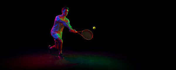 Competitive man, tennis athlete in motion during game, playing, practicing against dark background in neon light. Concept of professional sport, competition, game, math, hobby, action