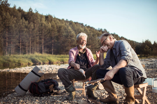 Two senior men camping in nature cooking fish