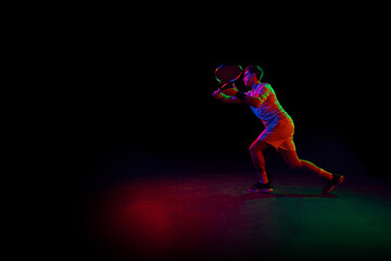 Competitive man, tennis athlete in motion during game, playing, practicing against dark background in neon light. Concept of professional sport, competition, game, math, hobby, action