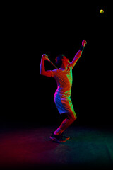 Fototapeta na wymiar Full-length of man in his 30s, tennis player during game, hitting ball with racket against dark background in neon light. Concept of professional sport, competition, game, math, hobby, action
