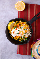 Esquites, grilled corn, served with grated cheese, sour cream, chili powder and slice of lemon in cast iron pan. Mexican street food meal. Top view