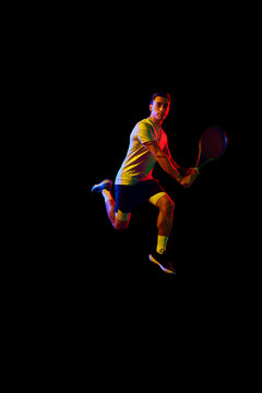 Dynamic image of man, tennis player in motion with racket against dark background in neon light. Concept of professional sport, competition, game, math, hobby, action