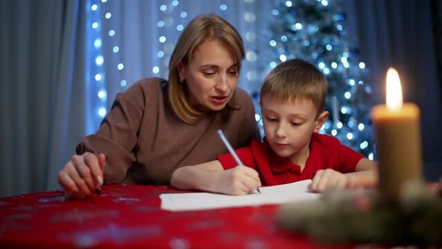 Mother and son, surrounded by a magical atmosphere, write a letter to Santa. A decorated Christmas tree, toys and lights create a festive mood in every word. High quality 4k footage